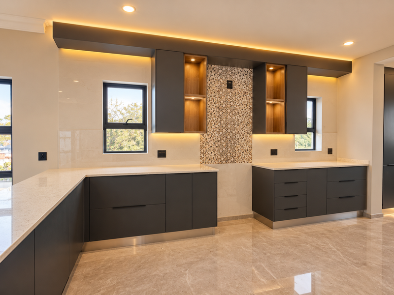 Modern kitchen featuring sleek dark cabinetry, quartz countertops, decorative tiled backsplash, and integrated ambient lighting with polished porcelain flooring.