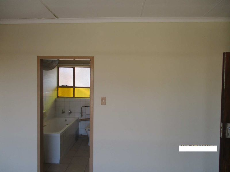 A view from an adjacent room into a dated bathroom featuring a bathtub, toilet, and tiled finishes, requiring cosmetic updates.