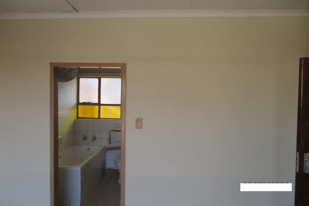 A view from an adjacent room into a dated bathroom featuring a bathtub, toilet, and tiled finishes, requiring cosmetic updates.