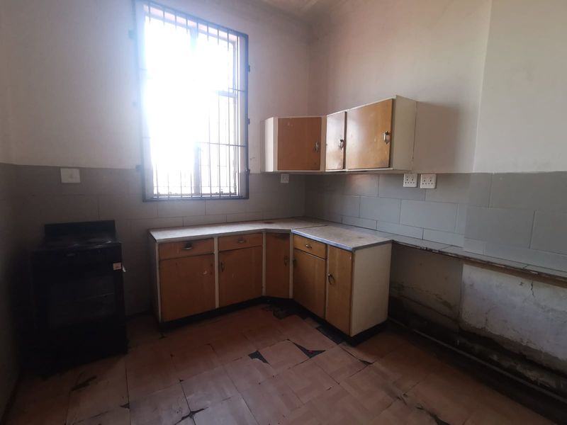 A dated, empty kitchen featuring original cabinetry, tiled splashbacks, and a window with security bars, requiring renovation to modernize the space.