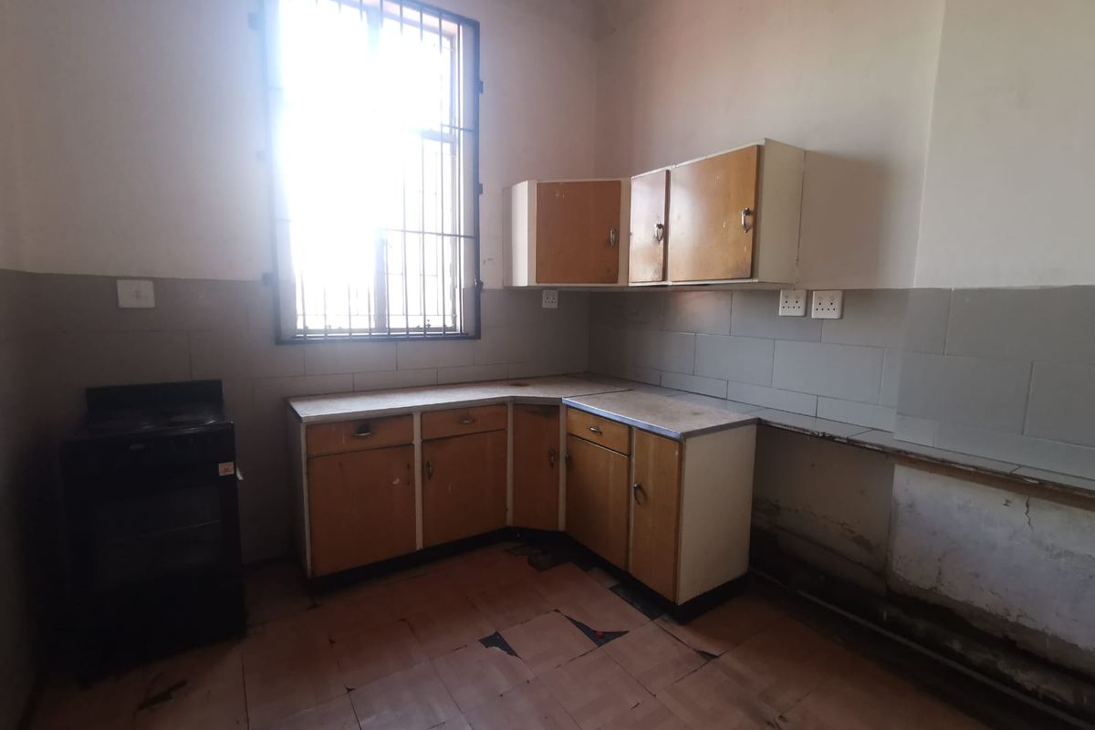A dated, empty kitchen featuring original cabinetry, tiled splashbacks, and a window with security bars, requiring renovation to modernize the space.