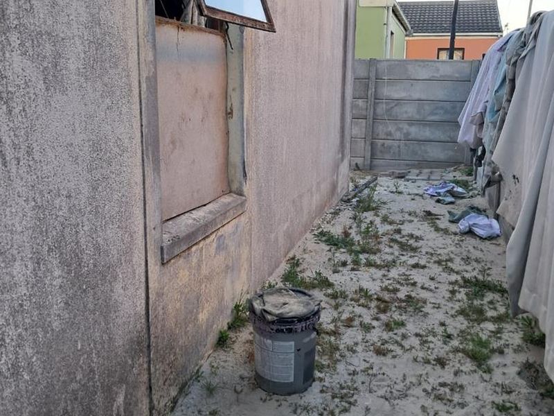 A view of the rear exterior wall showing a damaged window frame and unmaintained ground area with a precast concrete boundary wall.