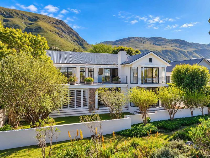 A well-maintained two-story residence featuring stone accents, a metal roof, and a balcony, set against a scenic mountain backdrop with landscaped gardens.