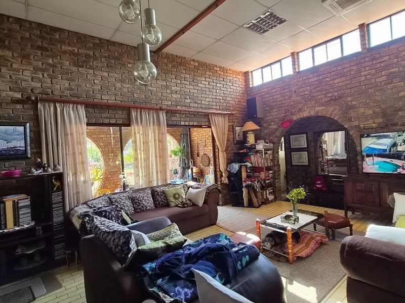 Spacious living room featuring exposed brick walls, high ceilings with clerestory windows, and large sliding glass doors providing natural light and garden access.
