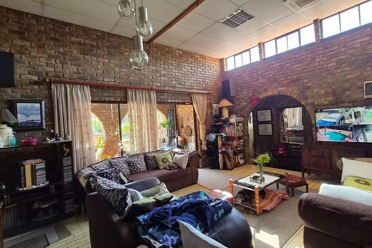 Spacious living room featuring exposed brick walls, high ceilings with clerestory windows, and large sliding glass doors providing natural light and garden access.