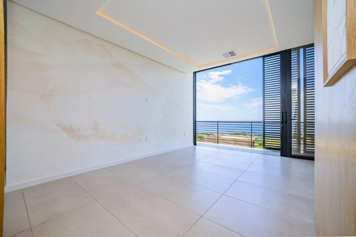 Bright bedroom featuring large sliding glass doors leading to a balcony with ocean views, recessed ceiling lighting, and neutral tiled flooring.