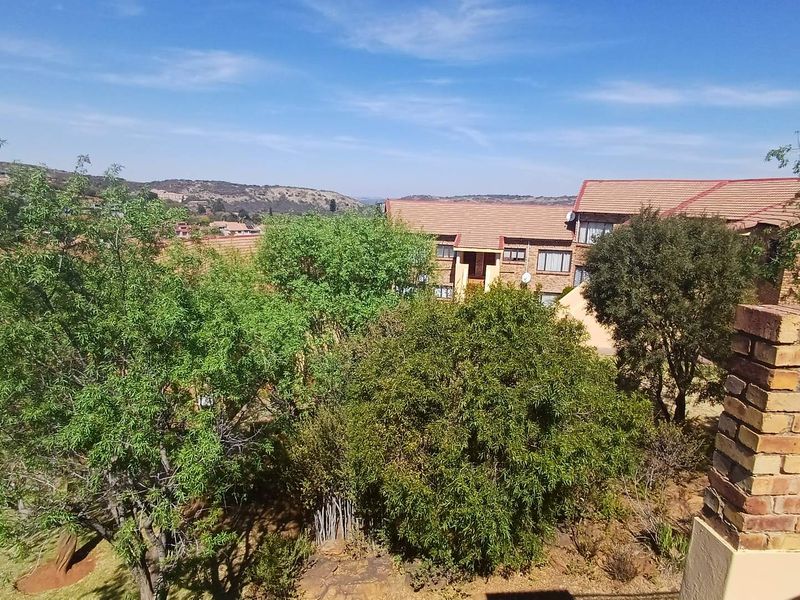 An elevated view overlooking the surrounding residential complex, mature trees, and distant landscape under a clear blue sky.