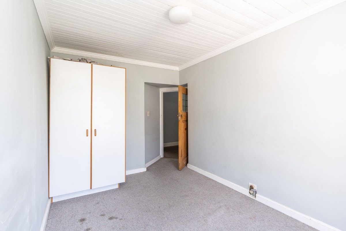 A bedroom featuring a built-in wardrobe, tongue and groove ceiling, and timber door, requiring minor repairs and flooring updates.
