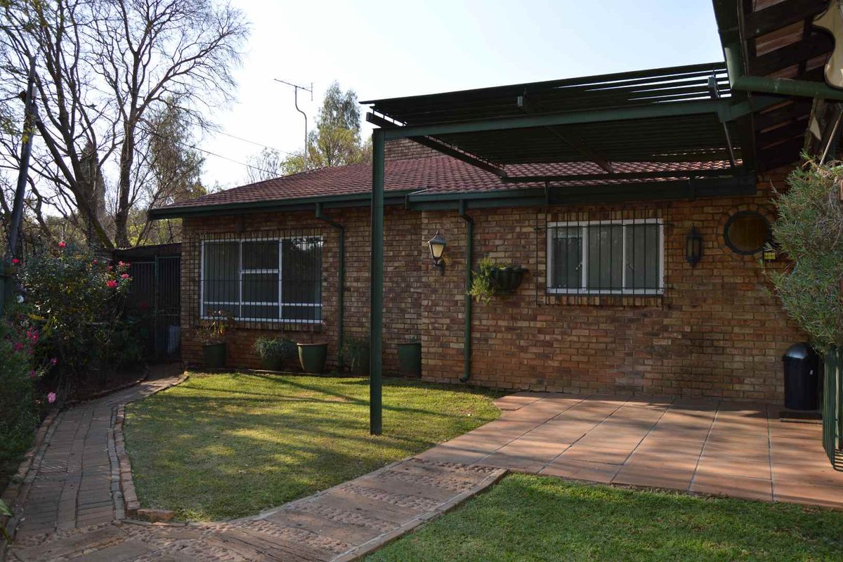 Rear view of a brick house featuring a covered patio area, paved garden pathways, and established landscaping.