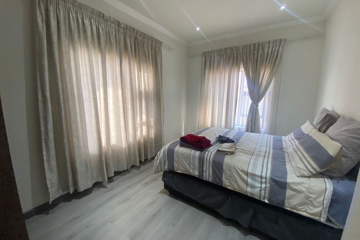 A well-maintained bedroom featuring light-toned laminate flooring, neutral walls, and dual windows fitted with curtain tracks and recessed ceiling lighting.