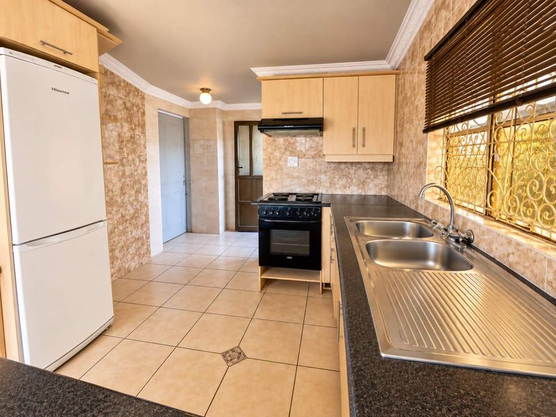 Functional kitchen featuring light wood cabinetry, dark laminate countertops, double stainless steel sink, and tiled finishes throughout.