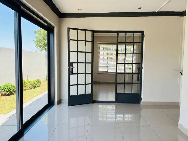 Bright and spacious living area featuring modern porcelain tile flooring, black steel-framed glass doors, and large sliding doors leading to the garden.