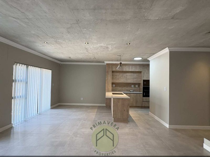 Spacious open-plan living area featuring a modern kitchen with built-in cabinetry, an island, and a unique exposed concrete ceiling with tiled flooring throughout.