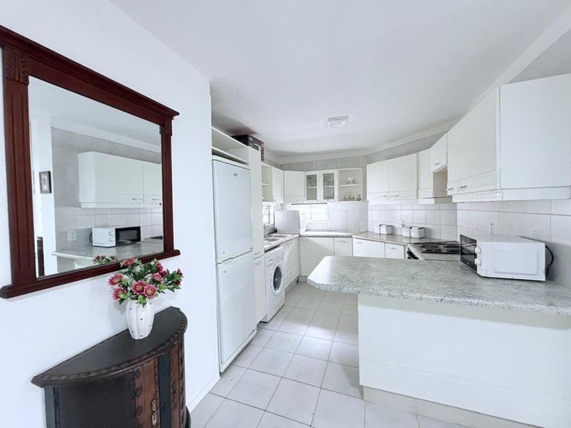 A functional kitchen featuring white cabinetry, laminate countertops, tiled backsplash, and a breakfast bar, providing a practical layout for daily cooking and dining.