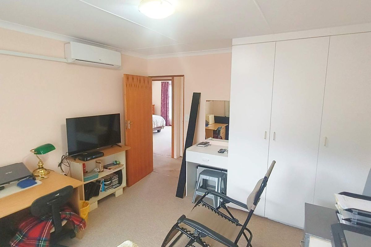 A functional bedroom featuring built-in white cabinetry, wall-mounted air conditioning unit, and carpeted flooring, with an adjoining doorway leading to another room.