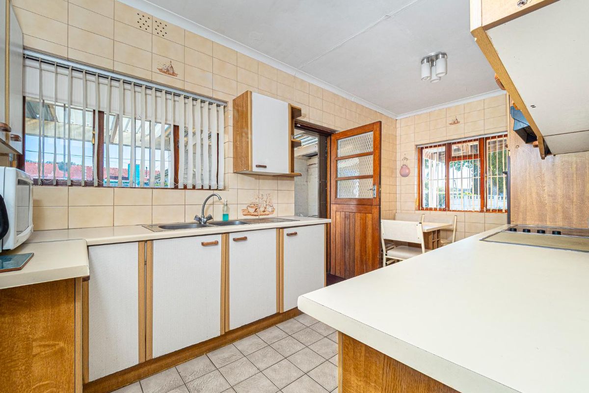 A functional kitchen featuring laminate countertops, built-in cabinetry, and ceramic tiling throughout, offering a dated aesthetic ready for modernization.