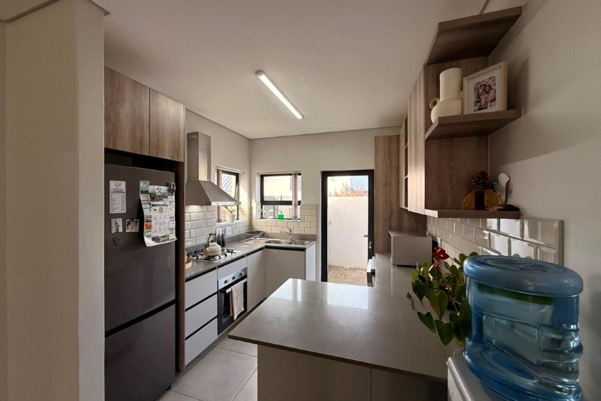 Modern kitchen featuring stone countertops, subway tile backsplash, built-in oven, extractor fan, and ample cabinetry with a breakfast bar area.