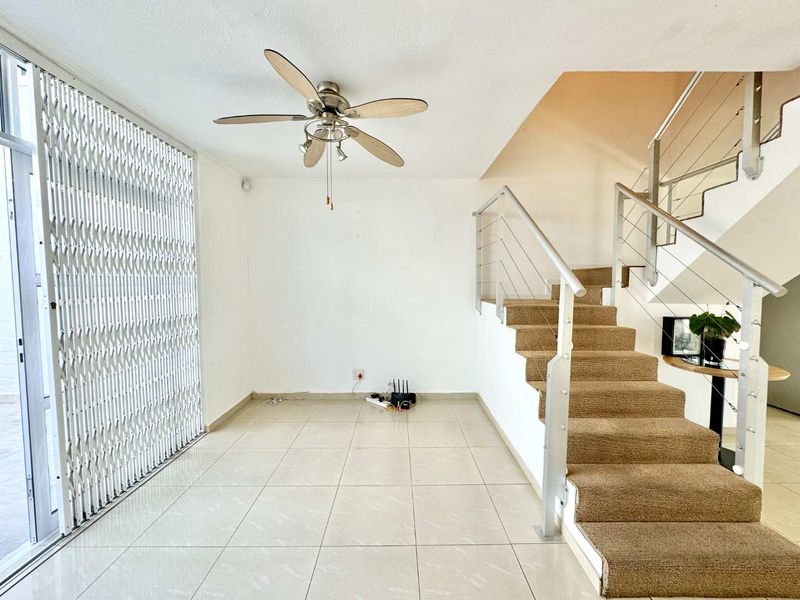 An open-plan living area featuring tiled flooring, a ceiling fan, and a staircase with a modern metal balustrade and security gate.