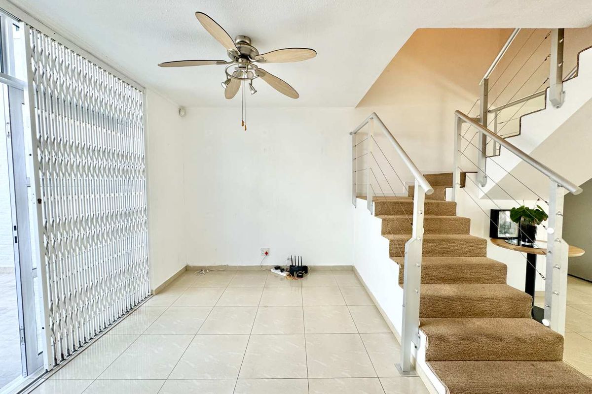 An open-plan living area featuring tiled flooring, a ceiling fan, and a staircase with a modern metal balustrade and security gate.