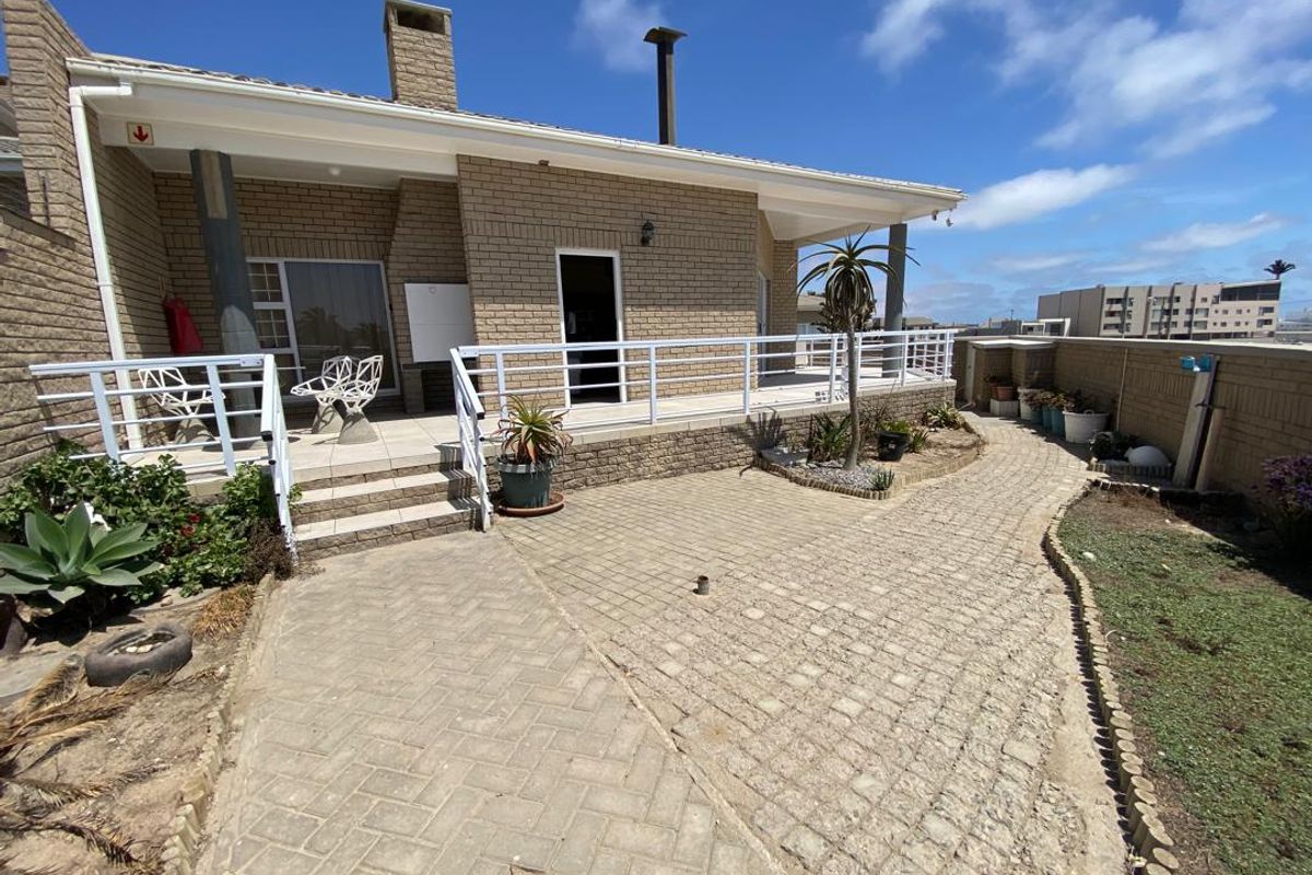A spacious rear patio area featuring paved walkways, a covered veranda, and brick exterior walls, offering a functional outdoor entertainment space.