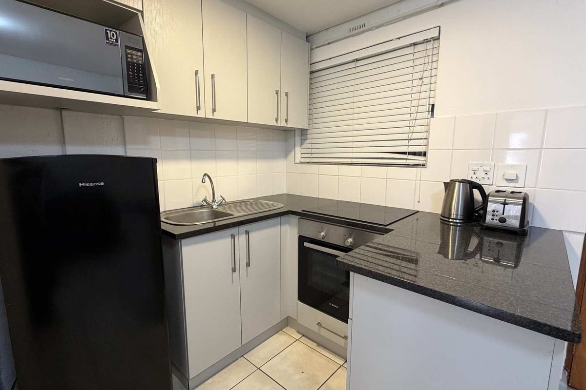 Compact kitchen featuring modern grey cabinetry, granite countertops, built-in oven, electric hob, and tiled finishes.