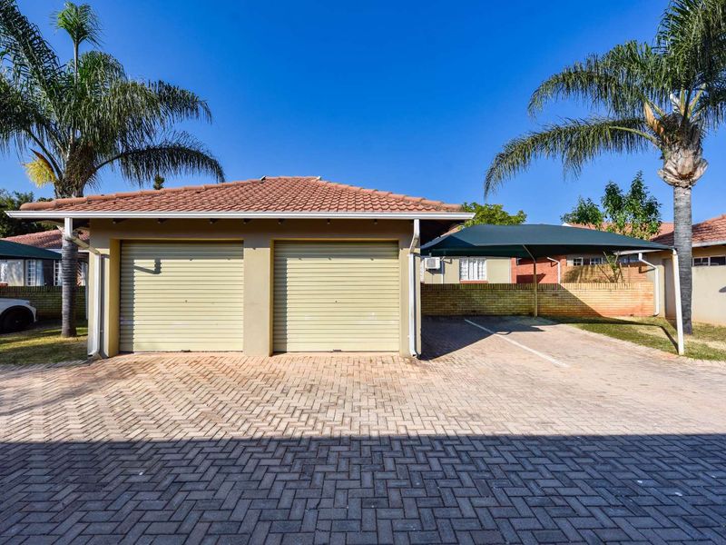Exterior view of a double garage with roll-up doors, featuring a paved driveway and an additional shade cloth carport area.