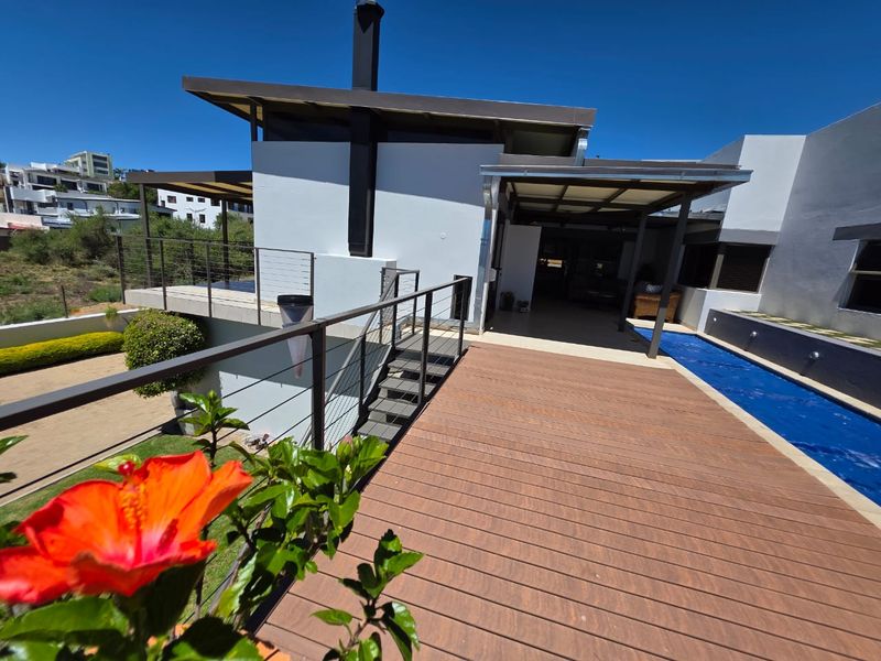 Rear exterior view featuring a modern wooden deck, swimming pool, and a covered patio area with metal staircase access.