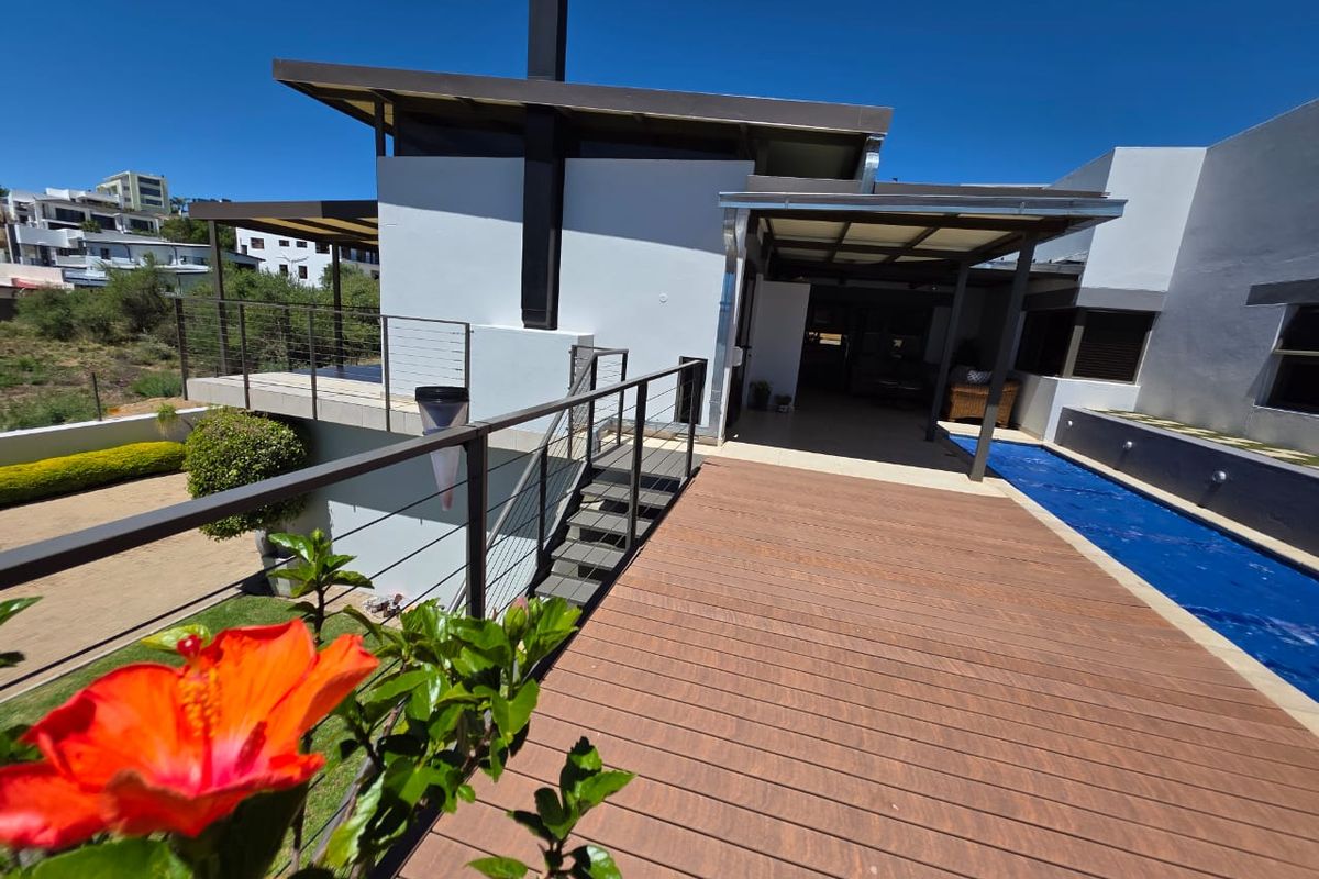 Rear exterior view featuring a modern wooden deck, swimming pool, and a covered patio area with metal staircase access.