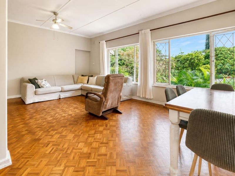 Spacious open-plan living and dining area featuring classic parquet flooring, a ceiling fan, and large windows providing ample natural light and garden views.