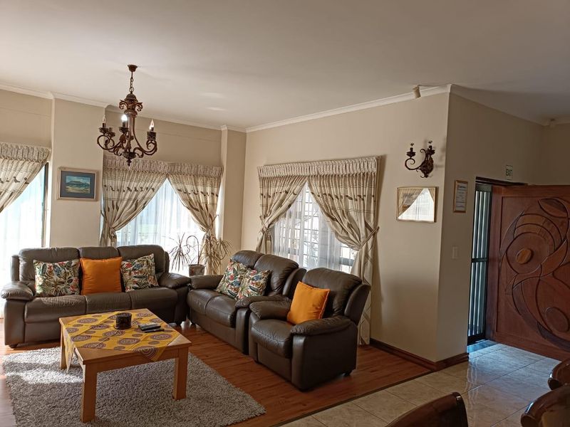 A spacious living room featuring a mix of laminate and tiled flooring, accented by traditional wrought iron lighting fixtures and a decorative wooden entrance door.