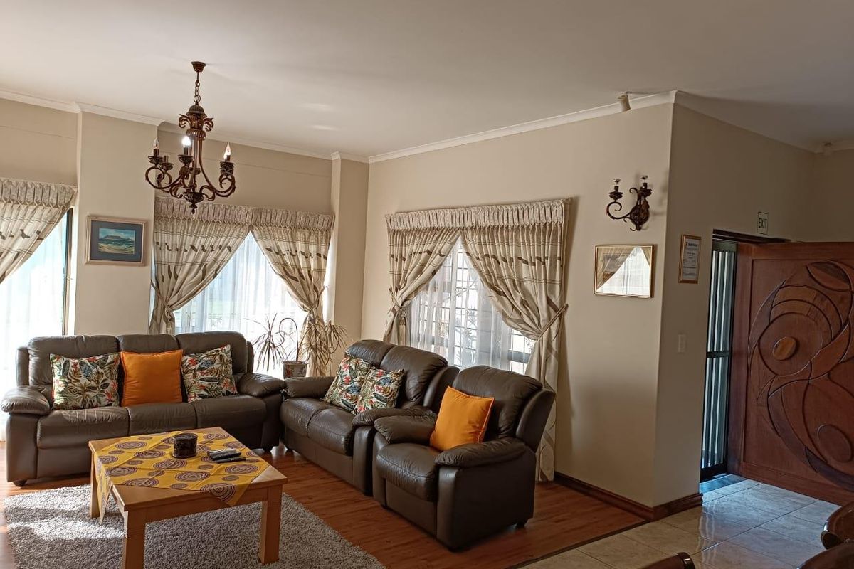 A spacious living room featuring a mix of laminate and tiled flooring, accented by traditional wrought iron lighting fixtures and a decorative wooden entrance door.