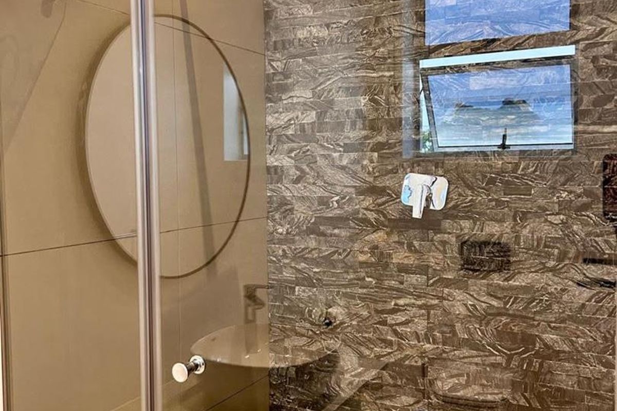 Modern bathroom shower enclosure featuring a stone-clad feature wall, mosaic floor tiling, and a contemporary rain shower head.