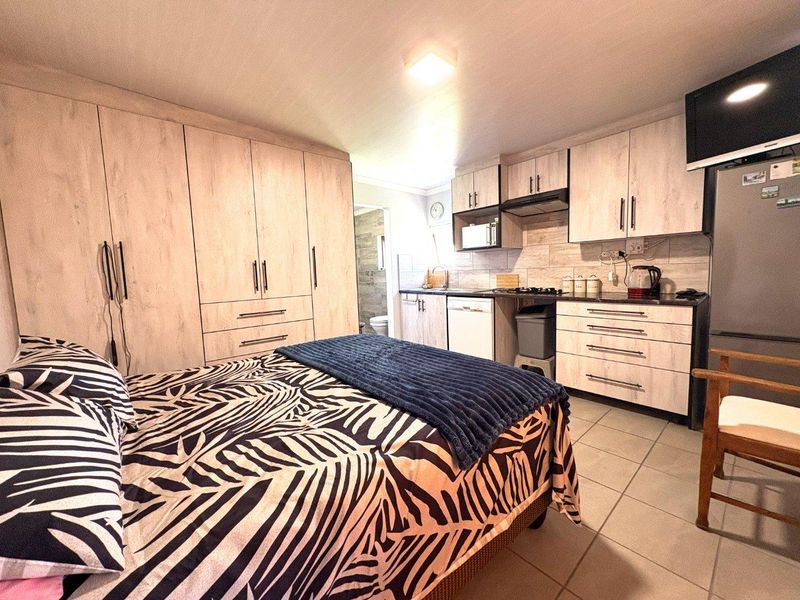 Compact open-plan studio space featuring a kitchenette with built-in cabinetry, hob, and extractor fan, alongside integrated storage cupboards and tiled flooring.