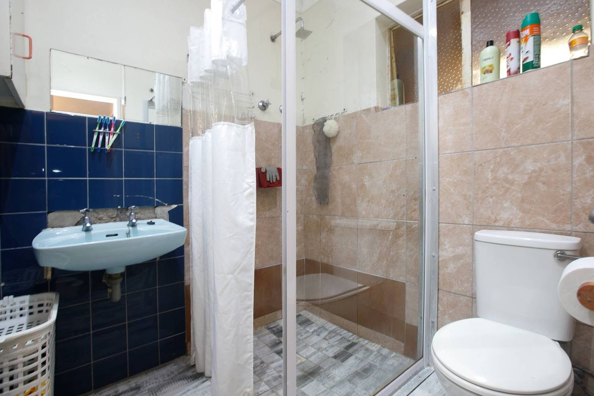 A functional bathroom featuring a shower enclosure, wall-mounted basin, and toilet, requiring cosmetic updates to modernize the space.