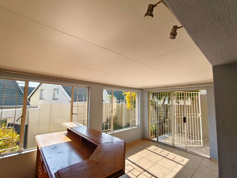A sunlit enclosed patio or sunroom featuring tiled flooring, large windows, and sliding door access to the exterior, suitable for a versatile living space.