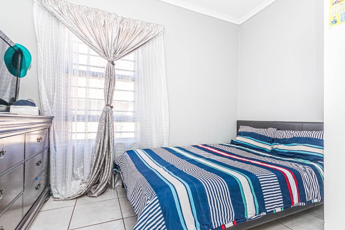A bedroom featuring tiled flooring and a window with security bars, providing a functional and well-lit sleeping space.