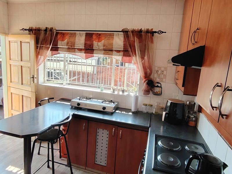 A functional kitchen featuring laminate cabinetry, dark countertops, a built-in electric hob, and an extractor fan, with direct access to the exterior.