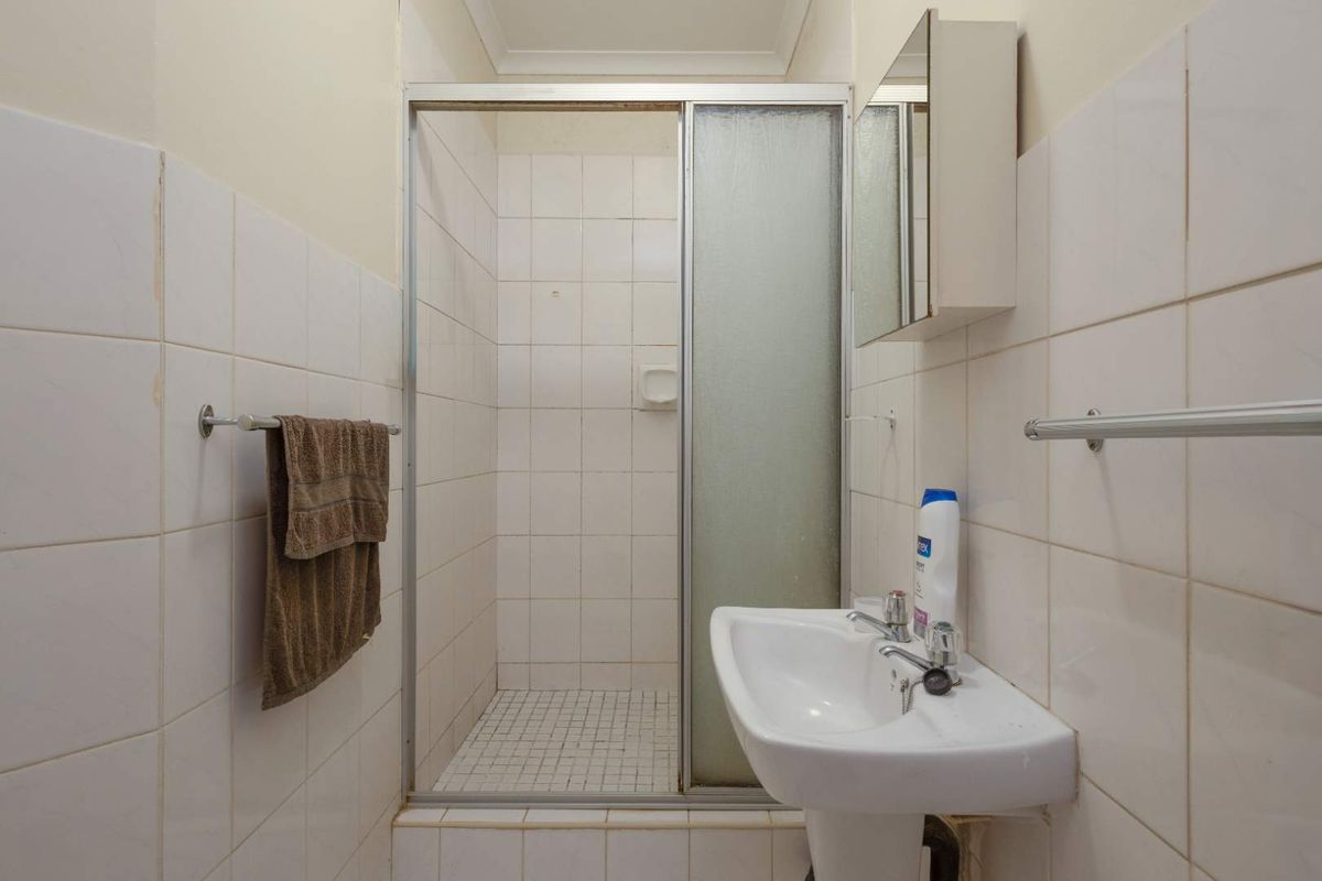 A compact bathroom featuring a shower enclosure, pedestal basin, and wall-mounted medicine cabinet with neutral wall tiling.
