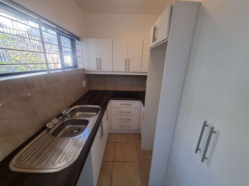 A compact, functional kitchen featuring white cabinetry, dark countertops, a double basin sink, and tiled flooring, offering a clean and efficient workspace.