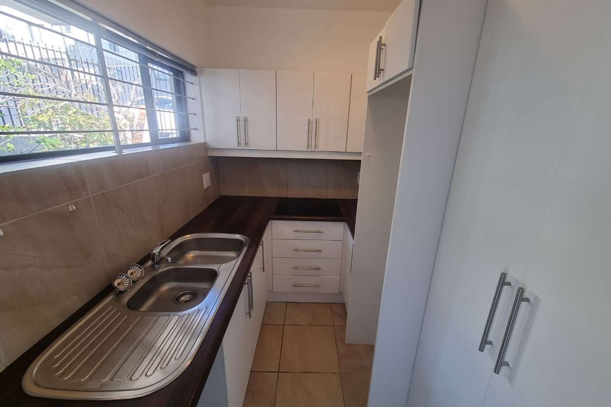 A compact, functional kitchen featuring white cabinetry, dark countertops, a double basin sink, and tiled flooring, offering a clean and efficient workspace.
