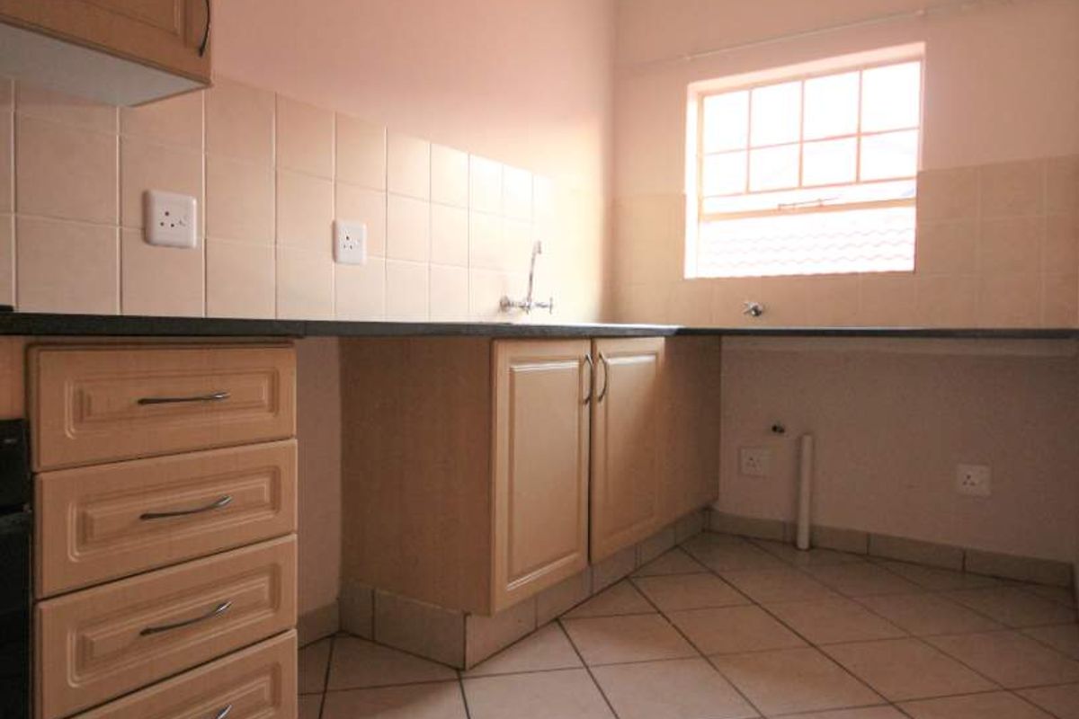 A functional, empty kitchen featuring built-in wooden cabinetry, tiled backsplash, and ceramic floor tiles, offering a clean canvas for potential updates.