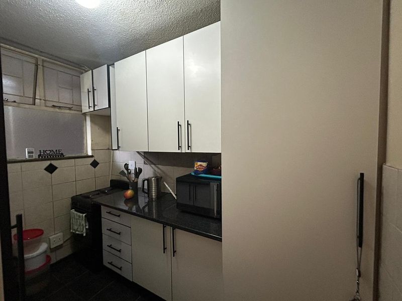 Compact kitchen featuring white cabinetry, dark stone-look countertops, tiled splashbacks, and a built-in stove area.