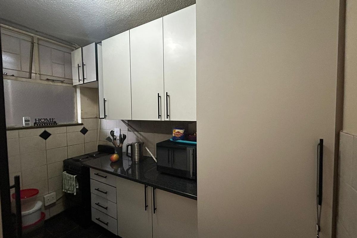 Compact kitchen featuring white cabinetry, dark stone-look countertops, tiled splashbacks, and a built-in stove area.