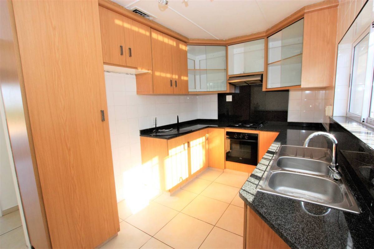 A functional kitchen featuring light wood-finish cabinetry, dark granite countertops, a double stainless steel sink, and built-in cooking appliances.