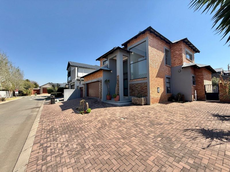 Modern double-story house featuring a brick and grey render facade, large feature window, and a spacious paved driveway with an integrated double garage.