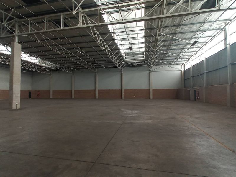 Spacious industrial warehouse featuring high ceilings with exposed steel trusses, concrete flooring, and natural light provided by integrated skylights.