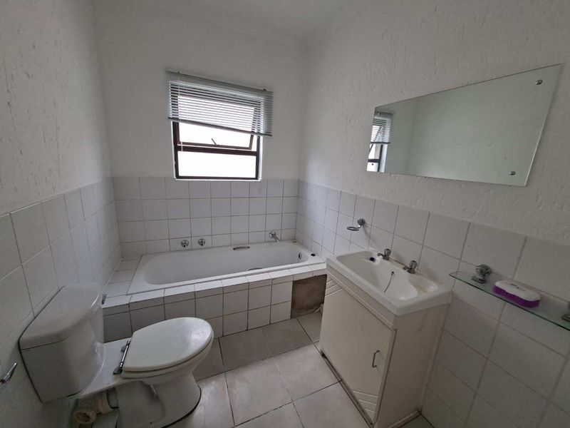 A functional bathroom featuring a built-in bathtub, vanity cabinet, and tiled finishes, offering a blank canvas for modernization and cosmetic updates.