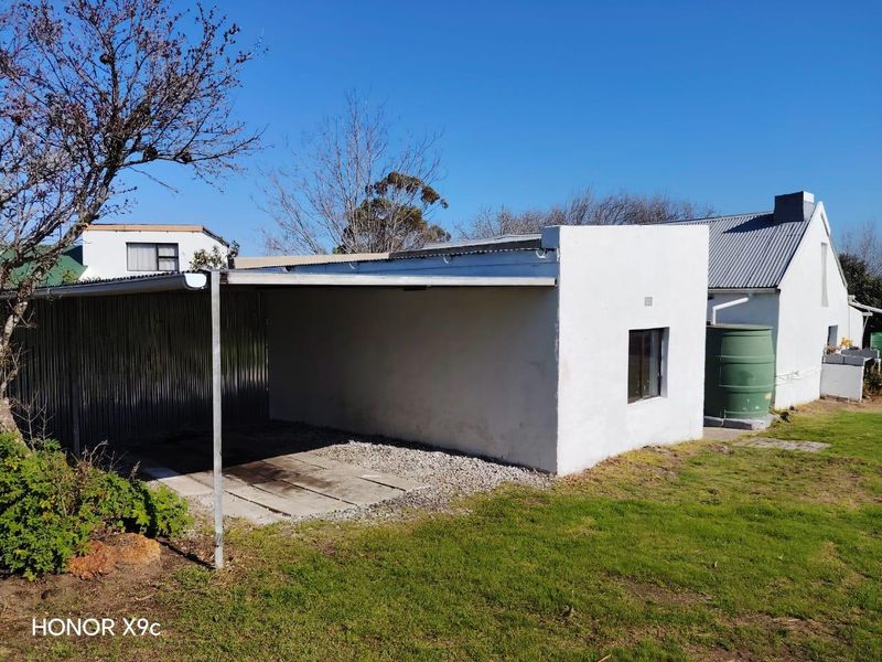 A detached garage or carport structure featuring a corrugated metal roof and an adjacent water storage tank set within a garden area.