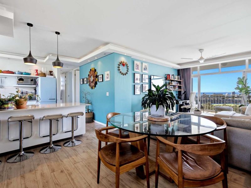 Bright open-plan living and dining area featuring a modern kitchen island, laminate flooring, and seamless access to a balcony with scenic views.
