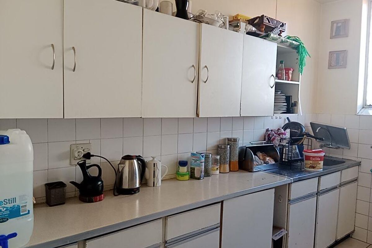 A functional kitchen featuring white cabinetry, laminate countertops, and a tiled backsplash, offering a practical layout with potential for modern updates.